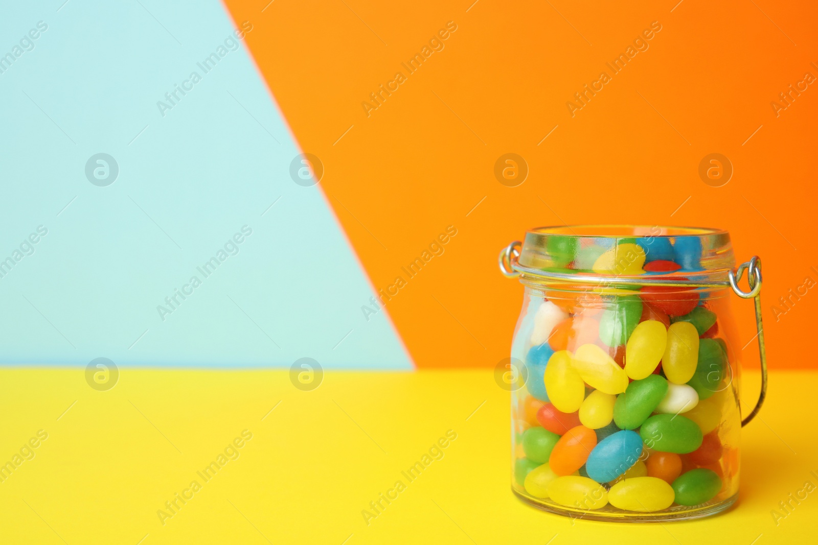 Photo of Jar of delicious jelly beans on color background. Space for text