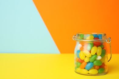 Photo of Jar of delicious jelly beans on color background. Space for text