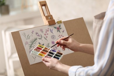 Photo of Woman painting flowers with watercolors in workshop, closeup