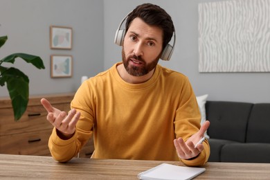Photo of Man in headphones talking to someone at wooden table indoors