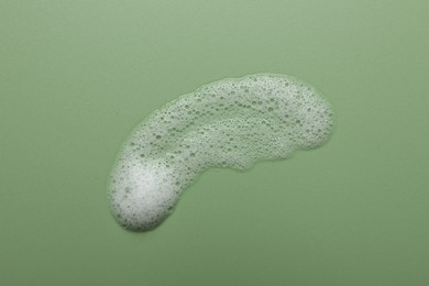 Photo of Smudge of fluffy soap foam on green background, top view