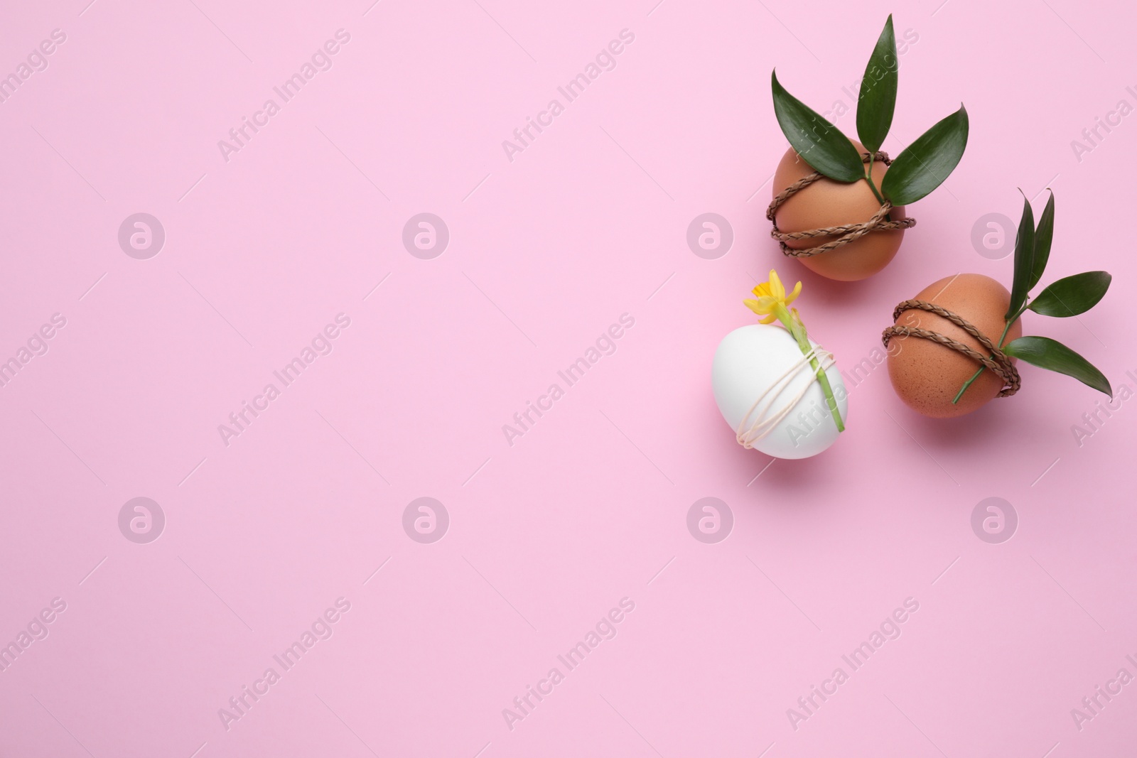 Photo of Easter eggs decorated with green leaves and flower on pink background, flat lay. Space for text