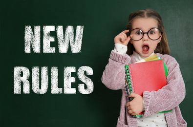 Image of Cute little child near text NEW RULES written on green board