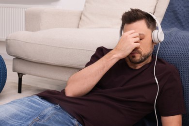 Upset man listening to music through headphones while lying on floor at home. Loneliness concept