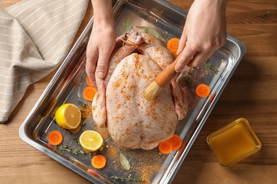Photo of Woman marinating whole turkey at table, top view