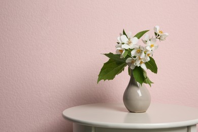 Photo of Beautiful bouquet with fresh jasmine flowers in vase on table near pink wall, space for text