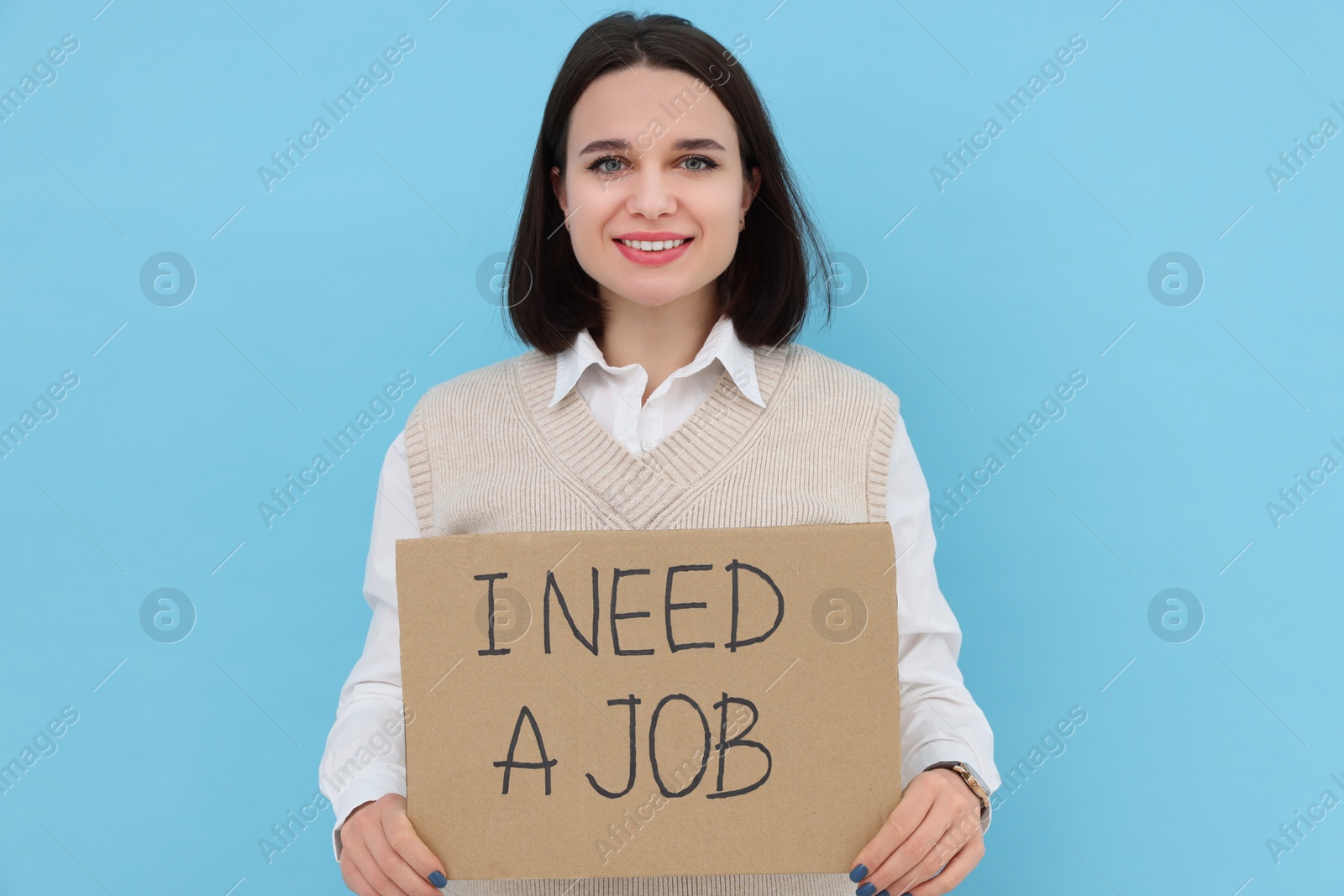 Photo of Happy young unemployed woman holding sign with phrase I Need A job on light blue background