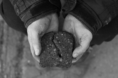 Photo of Poor homeless man holding piece of bread outdoors, top view. Black and white effect