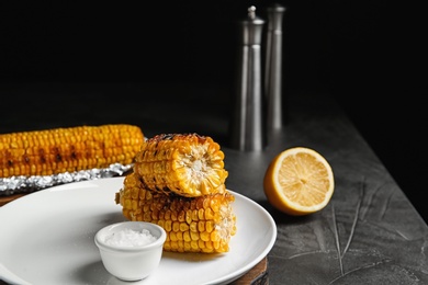 Photo of Plate with delicious grilled corn cobs and salt on gray table