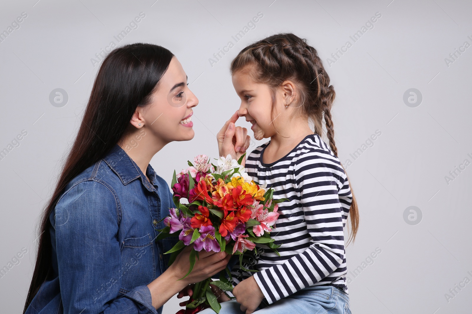 Photo of Happy woman with her cute daughter and bouquet of beautiful flowers on light grey background. Mother's day celebration