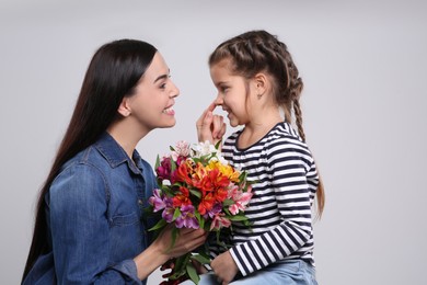 Happy woman with her cute daughter and bouquet of beautiful flowers on light grey background. Mother's day celebration