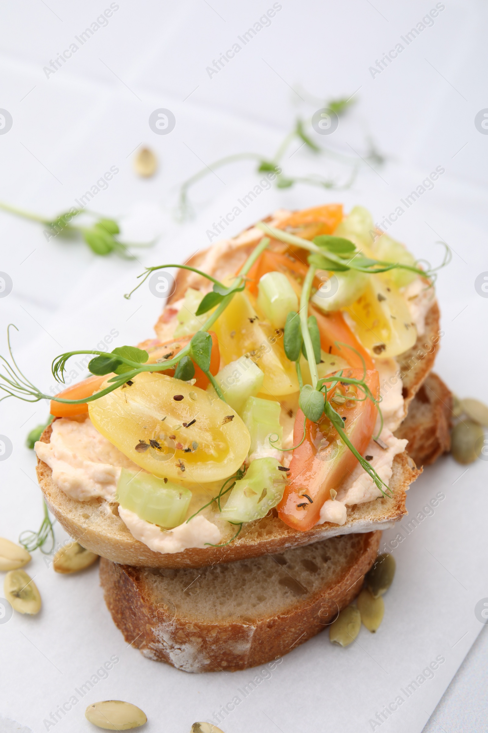 Photo of Tasty vegan sandwich with tomatoes, celery and microgreens on white tiled table, closeup