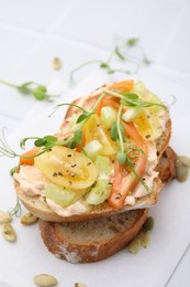 Tasty vegan sandwich with tomatoes, celery and microgreens on white tiled table, closeup