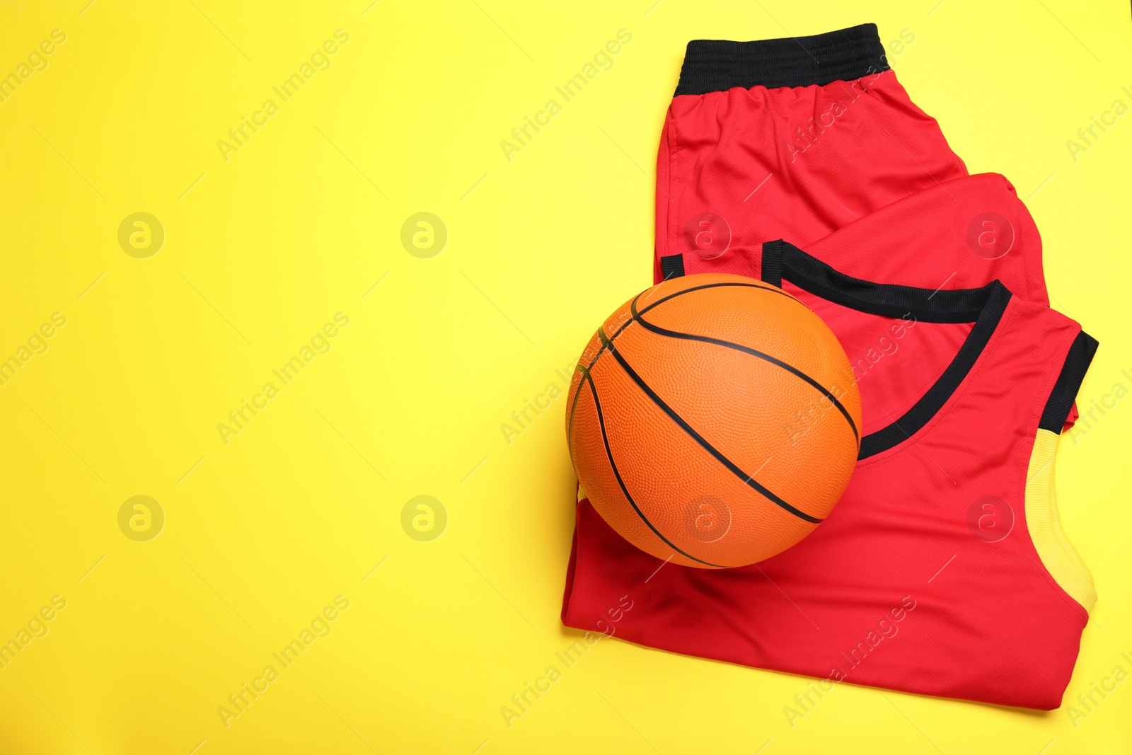 Photo of Basketball uniform and ball on yellow background, top view. Space for text