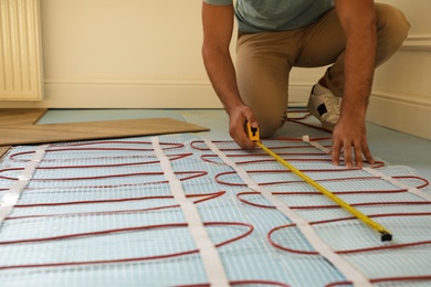 Photo of Professional worker installing electric underfloor heating system indoors, closeup