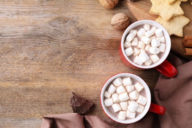 Flat lay composition of tasty cocoa with marshmallows on wooden table. Space for text