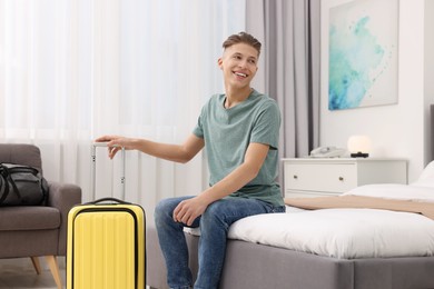 Photo of Smiling guest with suitcase relaxing on bed in stylish hotel room