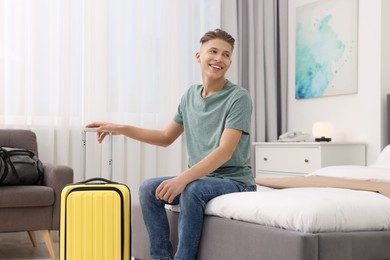 Smiling guest with suitcase relaxing on bed in stylish hotel room