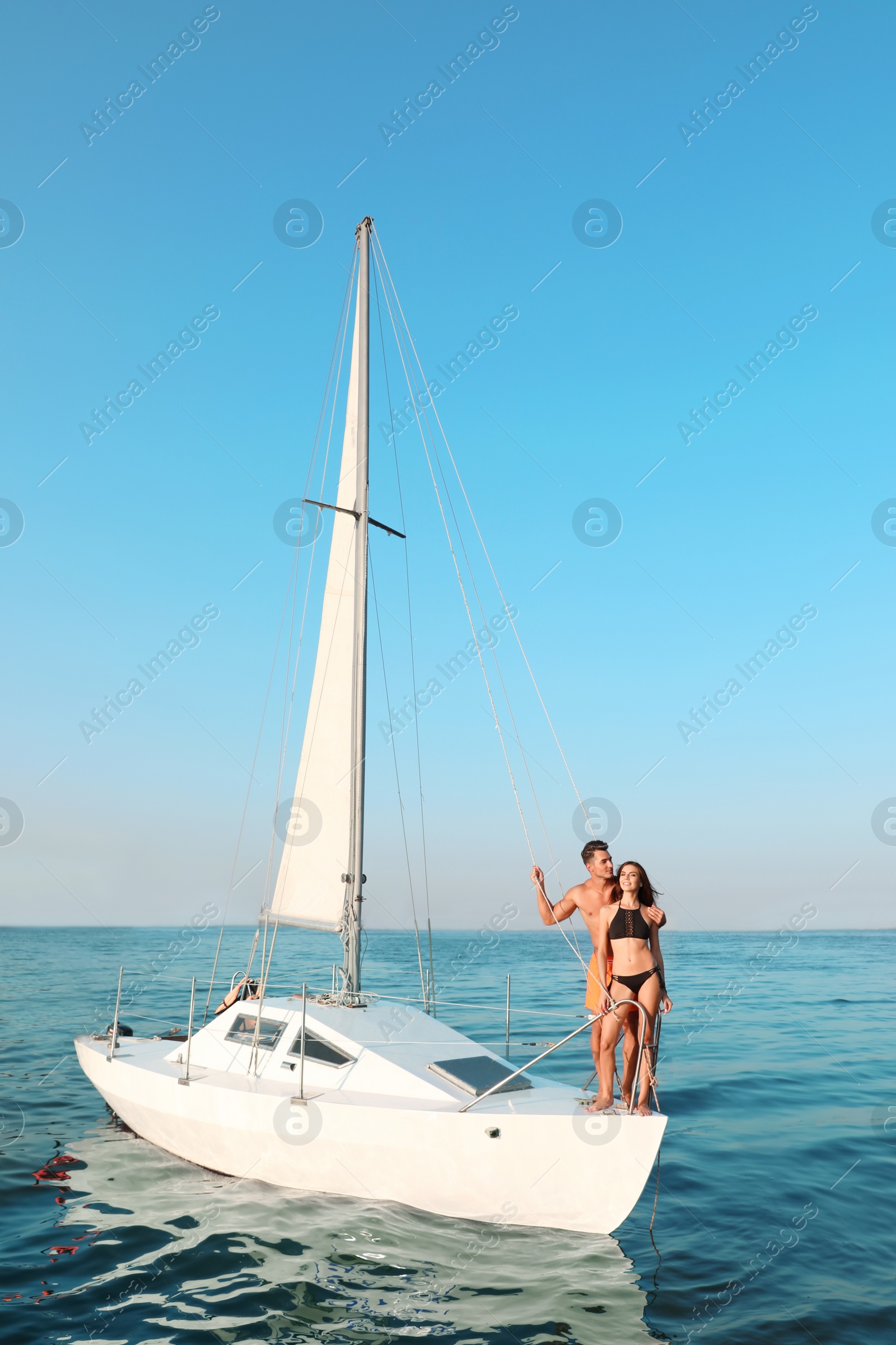 Photo of Young man and his beautiful girlfriend in bikini on yacht. Happy couple during sea trip