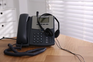 Photo of Stationary phone and headset on wooden table indoors. Hotline service