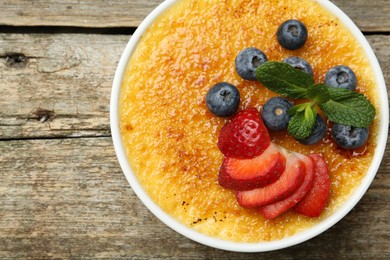 Delicious creme brulee with berries and mint in bowl on wooden table, top view. Space for text