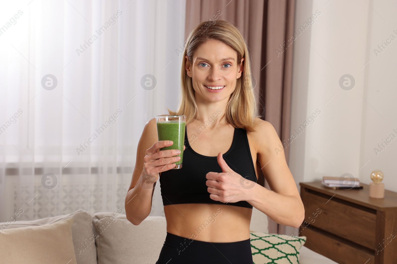 Photo of Young woman in sportswear with glass of fresh smoothie at home