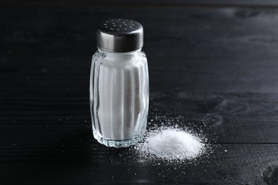 Photo of Organic salt in glass shaker on black wooden table, closeup