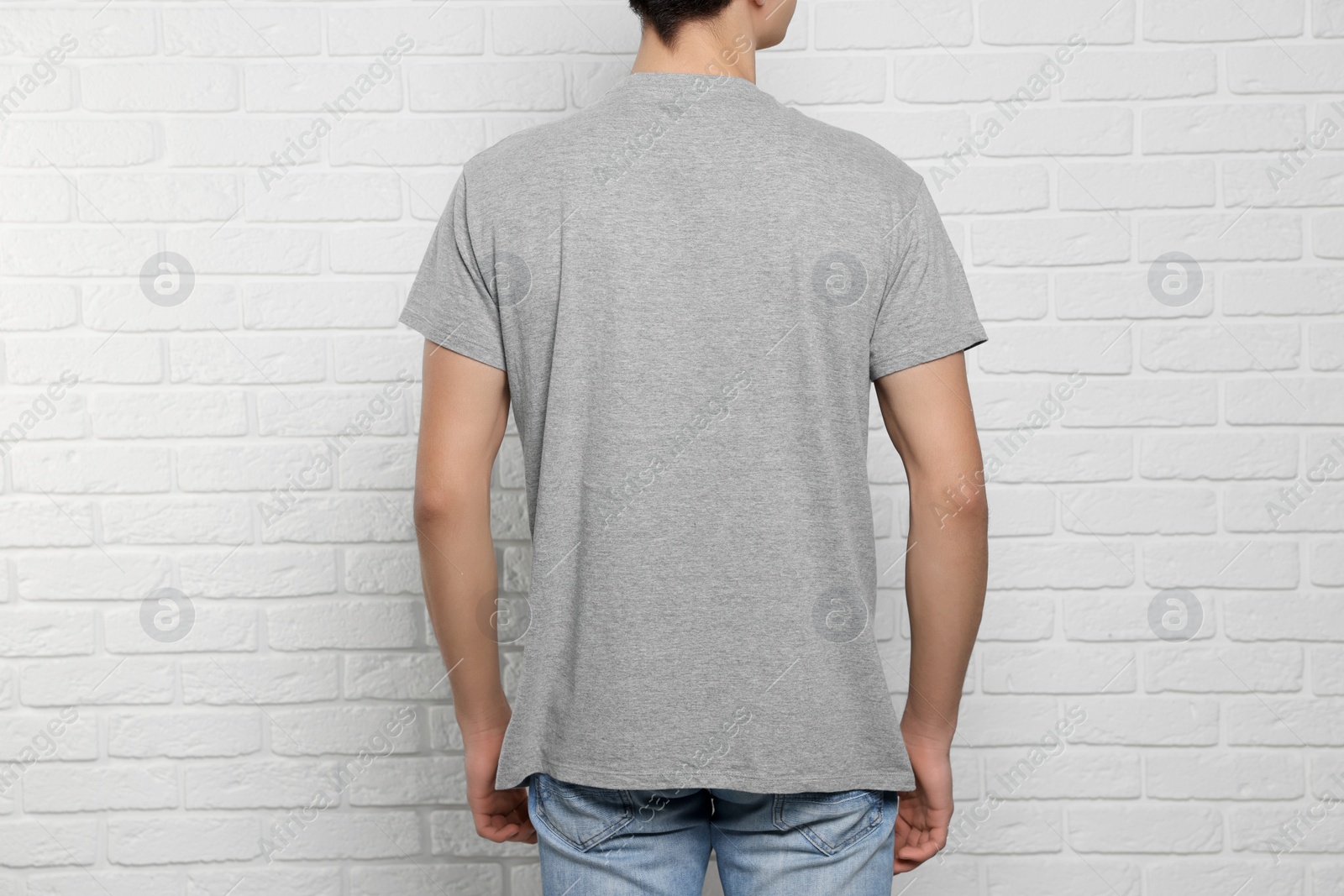 Photo of Man wearing gray t-shirt near white brick wall, back view. Mockup for design