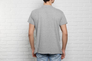 Photo of Man wearing gray t-shirt near white brick wall, back view. Mockup for design