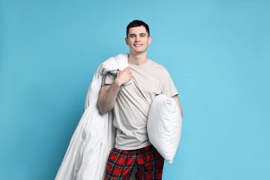 Happy man in pyjama holding blanket and pillow on light blue background