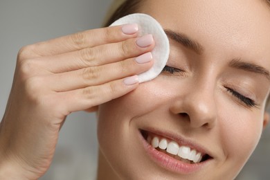 Photo of Smiling woman removing makeup with cotton pad on blurred background, closeup