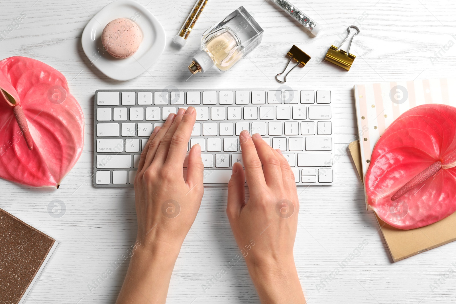 Photo of Woman using computer keyboard on wooden table decorated with tropical flowers, top view. Creative design ideas