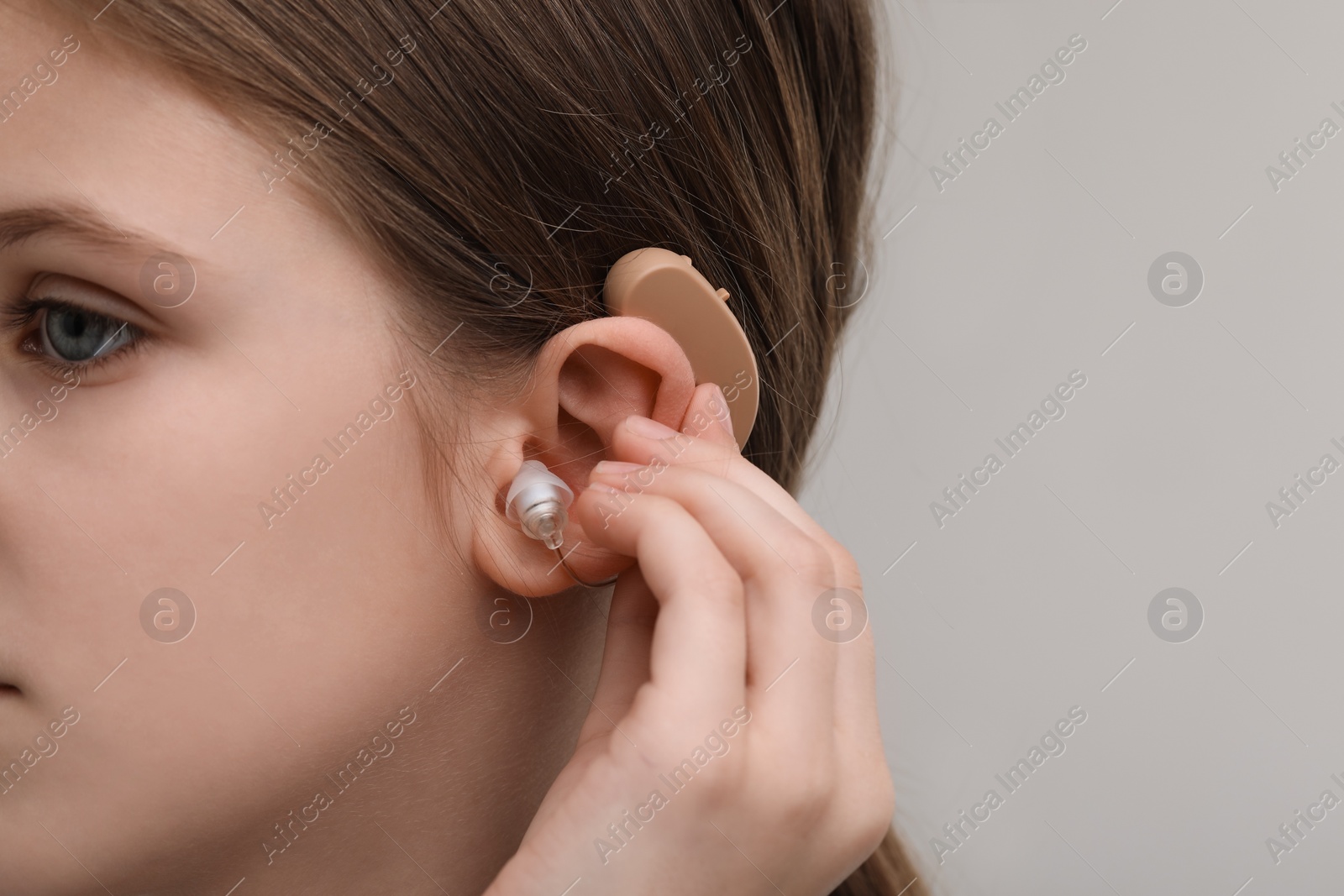 Photo of Little girl with hearing aid on grey background, closeup