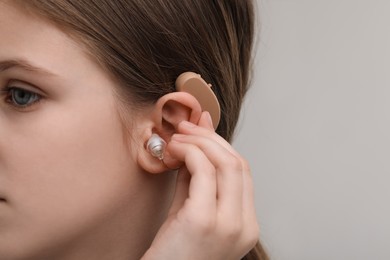 Little girl with hearing aid on grey background, closeup