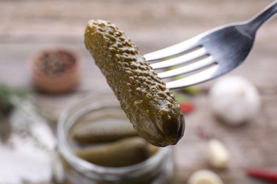 Photo of Fork with tasty pickled cucumber over jar on table, closeup