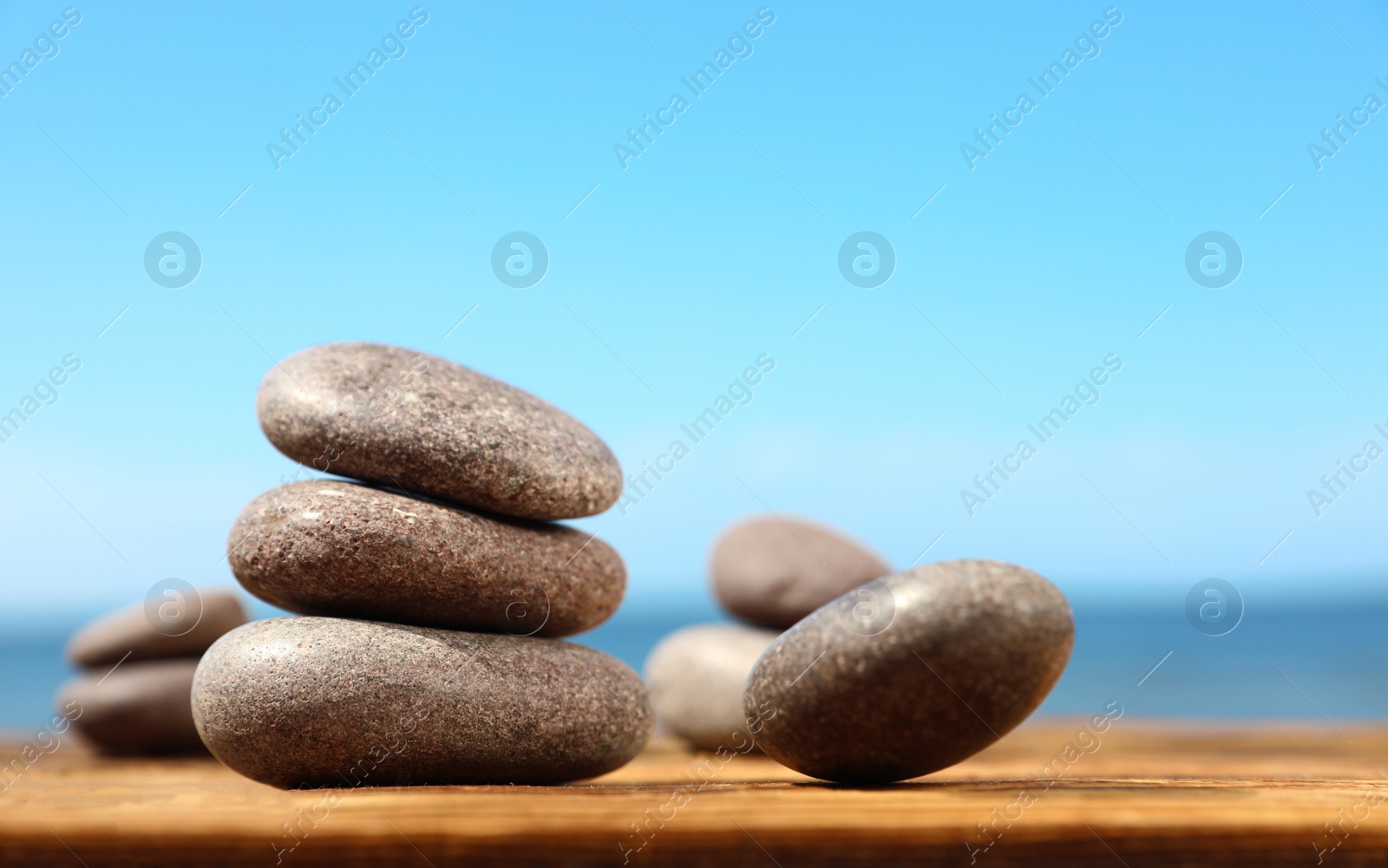 Photo of Stones on wooden table against seascape, space for text. Zen concept