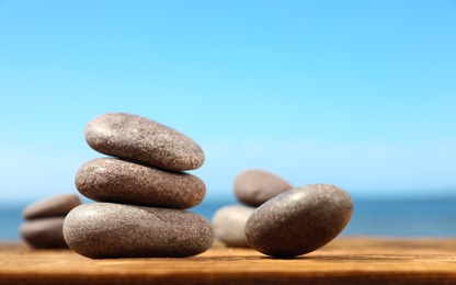 Photo of Stones on wooden table against seascape, space for text. Zen concept