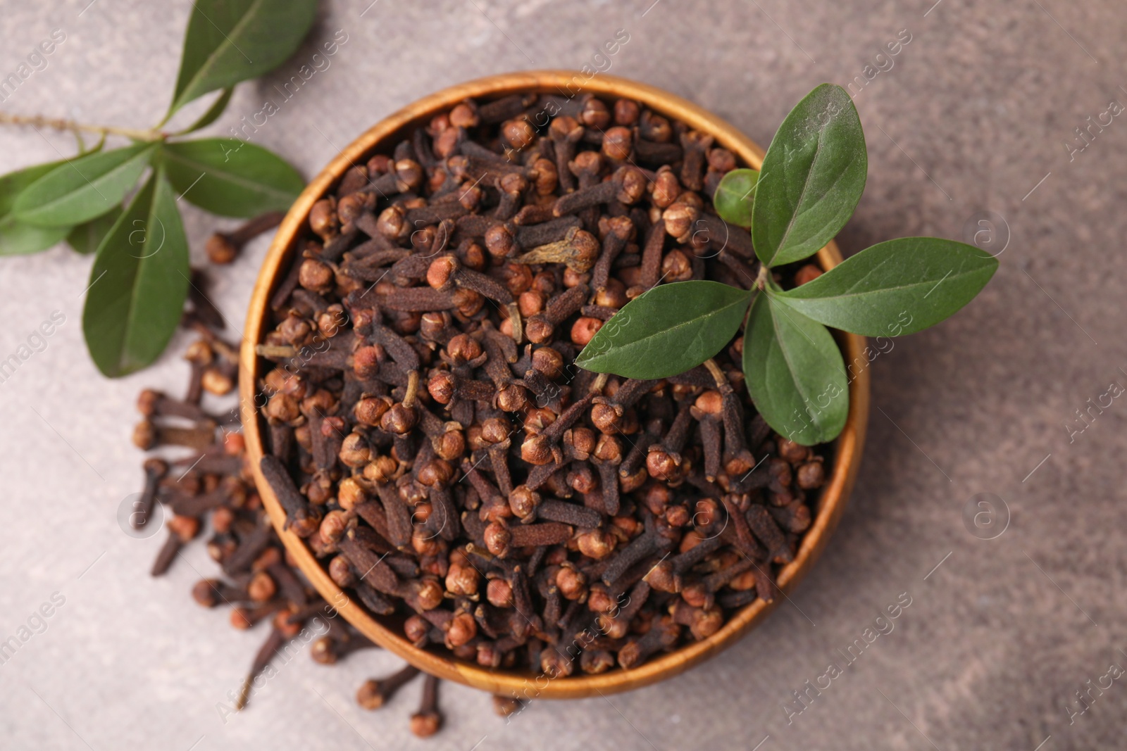 Photo of Aromatic cloves and green leaves in bowl on brown table, top view