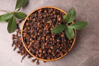 Aromatic cloves and green leaves in bowl on brown table, top view