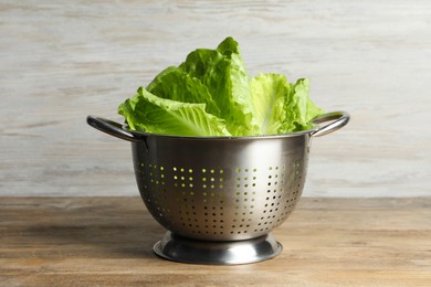 Photo of Colander with fresh leaves of green romaine lettuce on wooden table