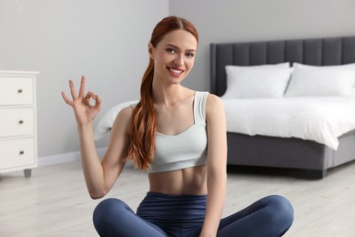 Photo of Young woman in sportswear showing OK gesture in bedroom