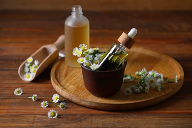 Photo of Chamomile essential oil and flowers on wooden table