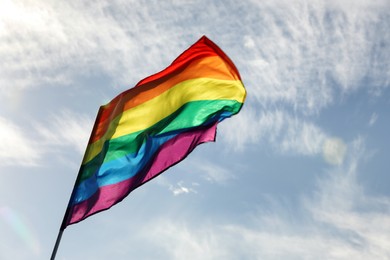 Bright LGBT flag against blue sky with clouds, space for text