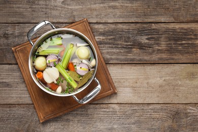 Photo of Different ingredients for cooking tasty bouillon in pot on wooden table, top view. Space for text