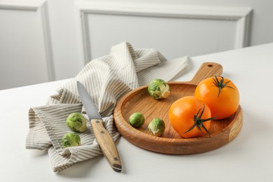 Photo of Cutting board with Brussels sprouts, tomatoes and knife on white wooden table