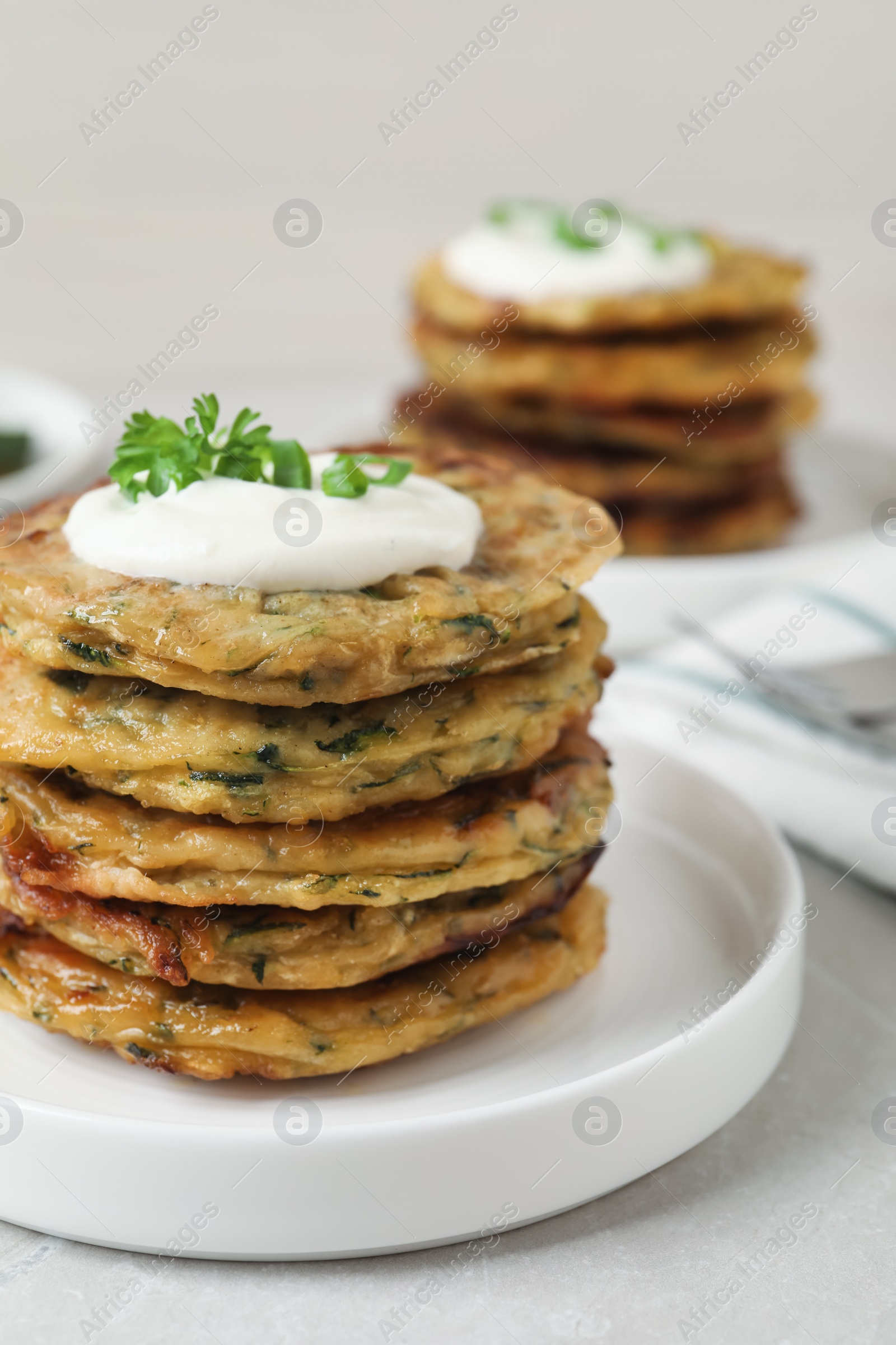 Photo of Delicious zucchini pancakes with sour cream served on light grey table, closeup