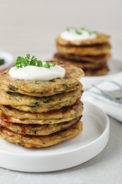 Photo of Delicious zucchini pancakes with sour cream served on light grey table, closeup