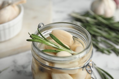 Photo of Jar of pickled garlic on marble table, closeup