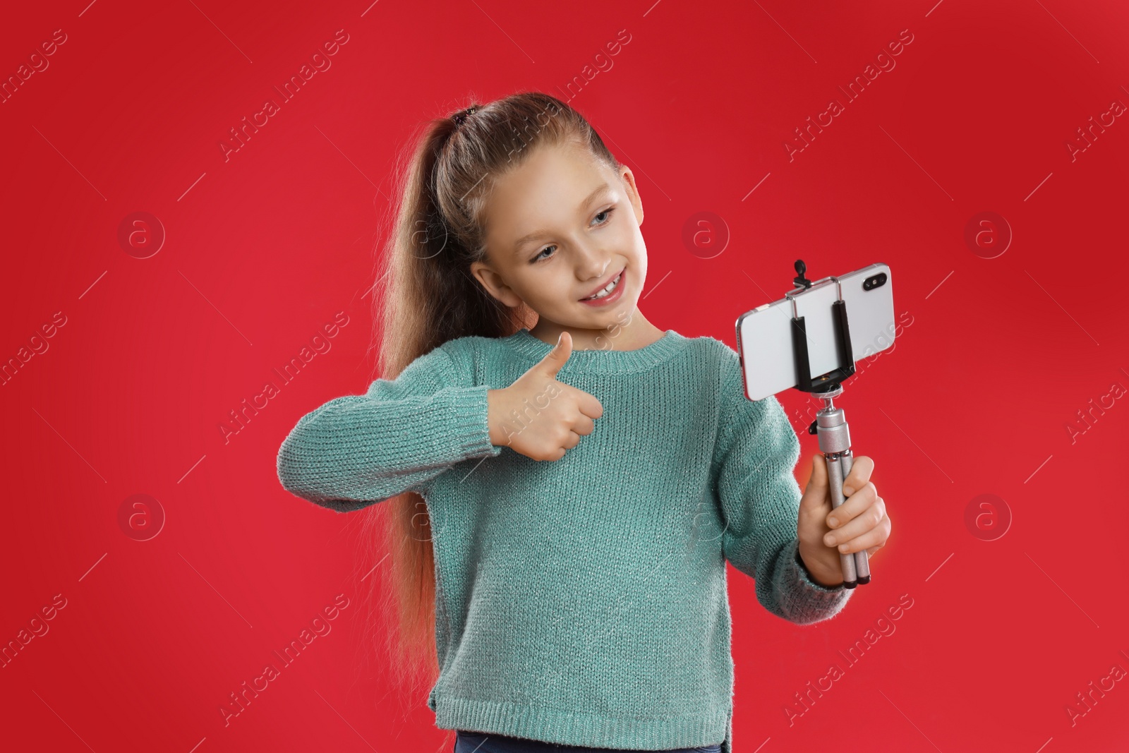 Photo of Cute little blogger recording video on red background