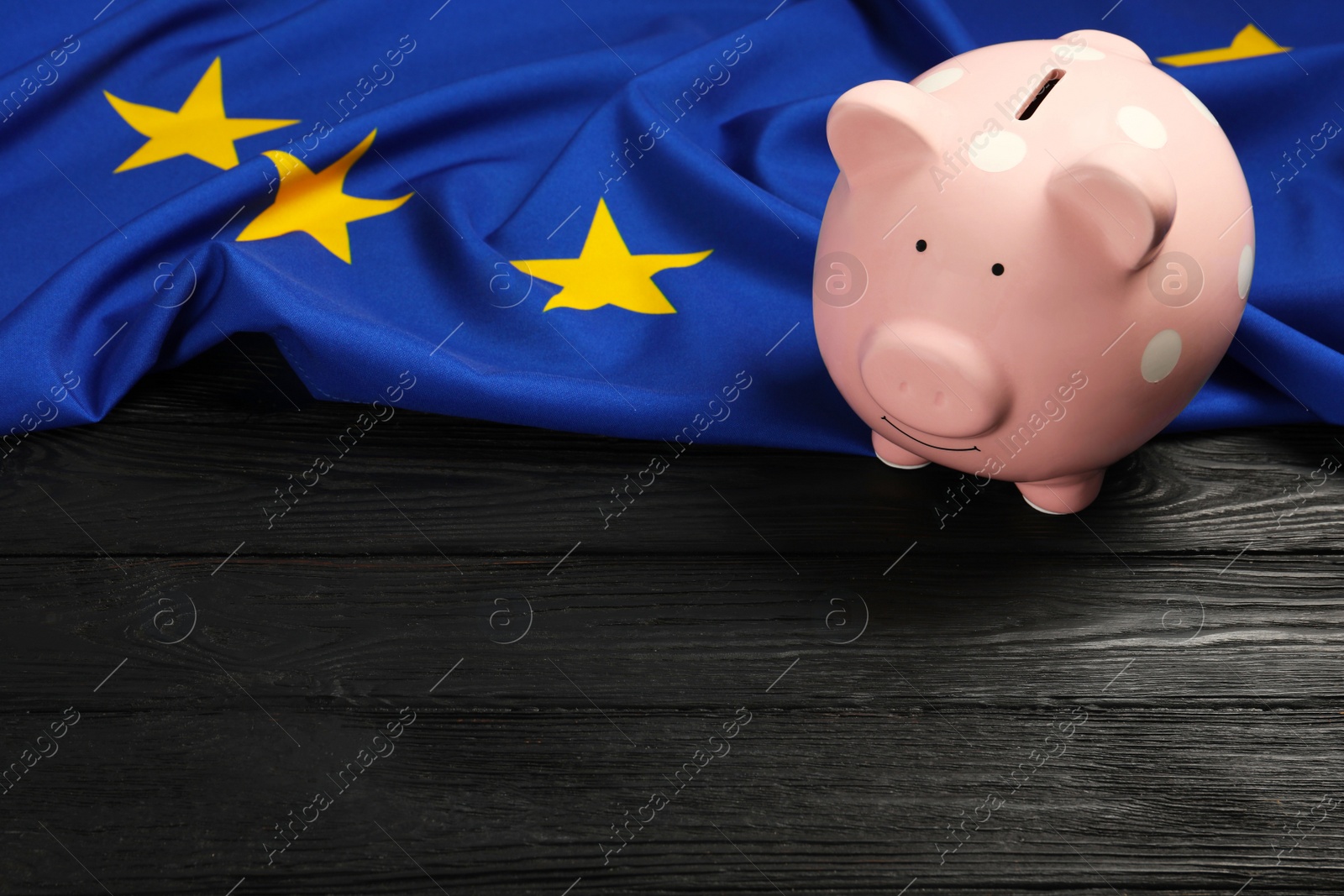 Photo of Pink piggy bank and flag of European Union on black wooden table. Space for text